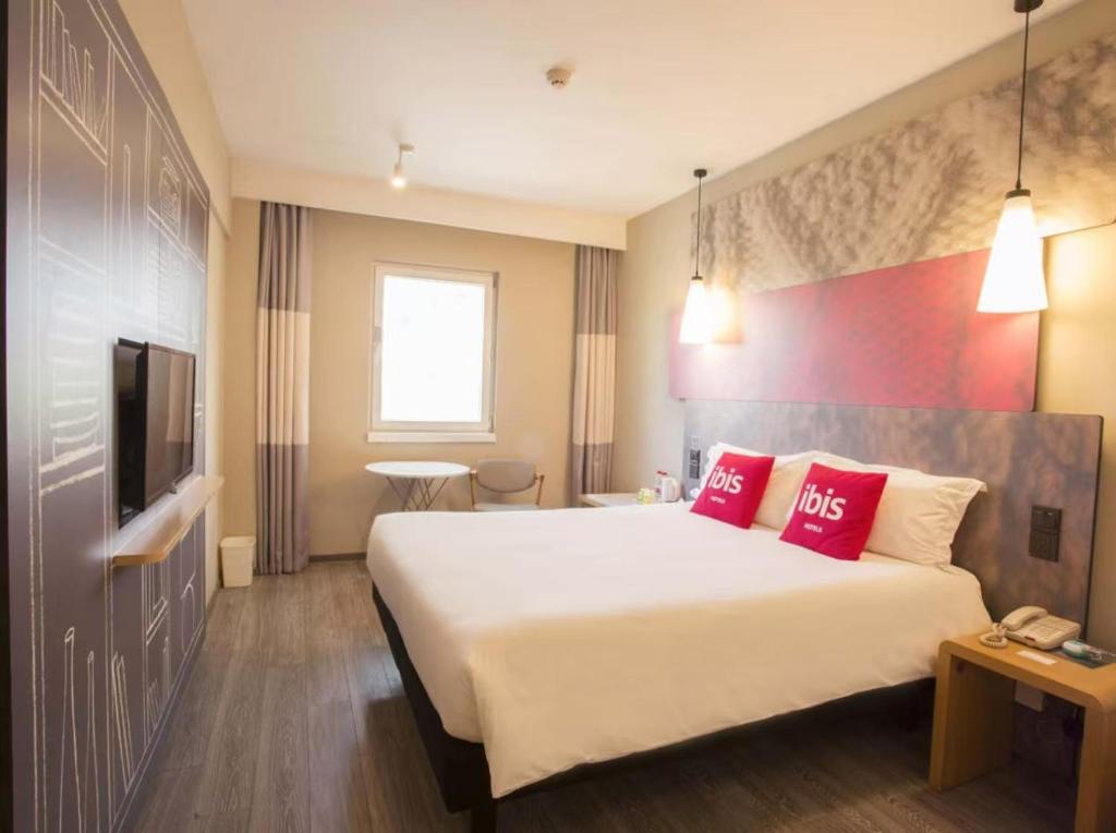 a hotel room with a large bed with red pillows at Ibis Tianjin Development Zone TEDA Third Avenue in Binhai