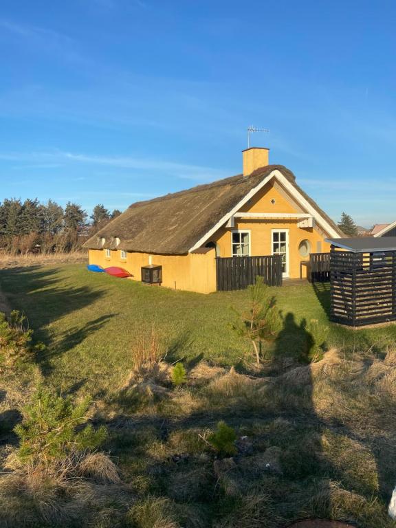 a yellow house with a black roof on a field at Viking Surf Cottage in Klitmøller