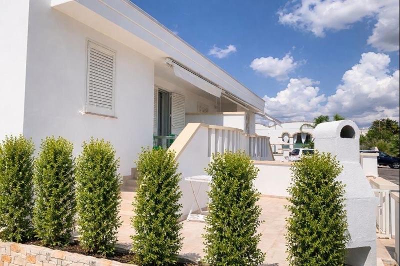a white house with a row of green bushes at Salentipity in Marina di Pescoluse
