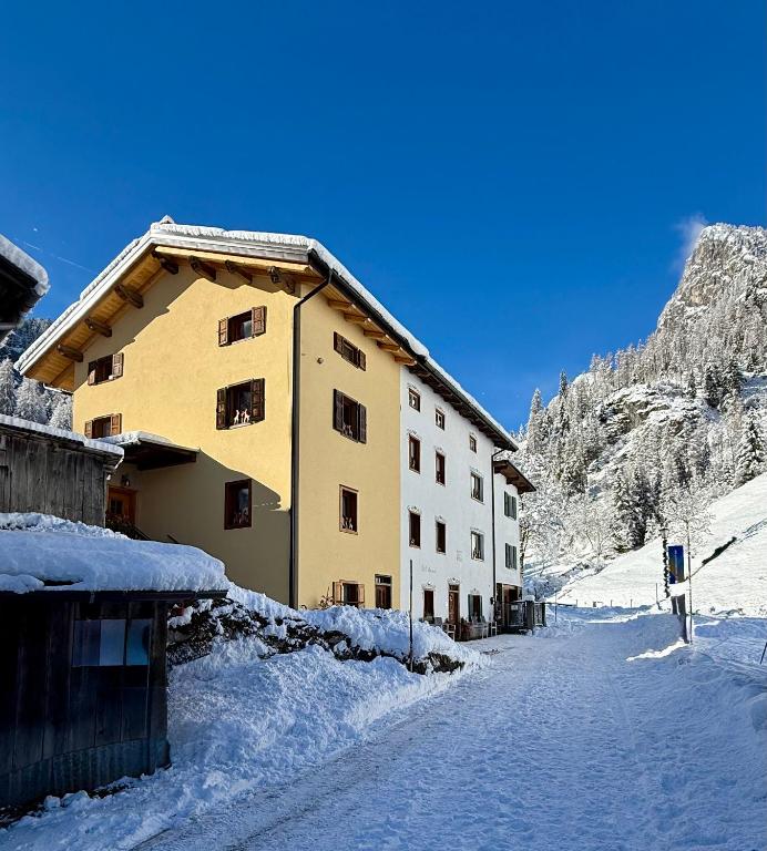 a building with snow on the ground next to a mountain at B&B Ciesa la Vèrda in Rocca Pietore