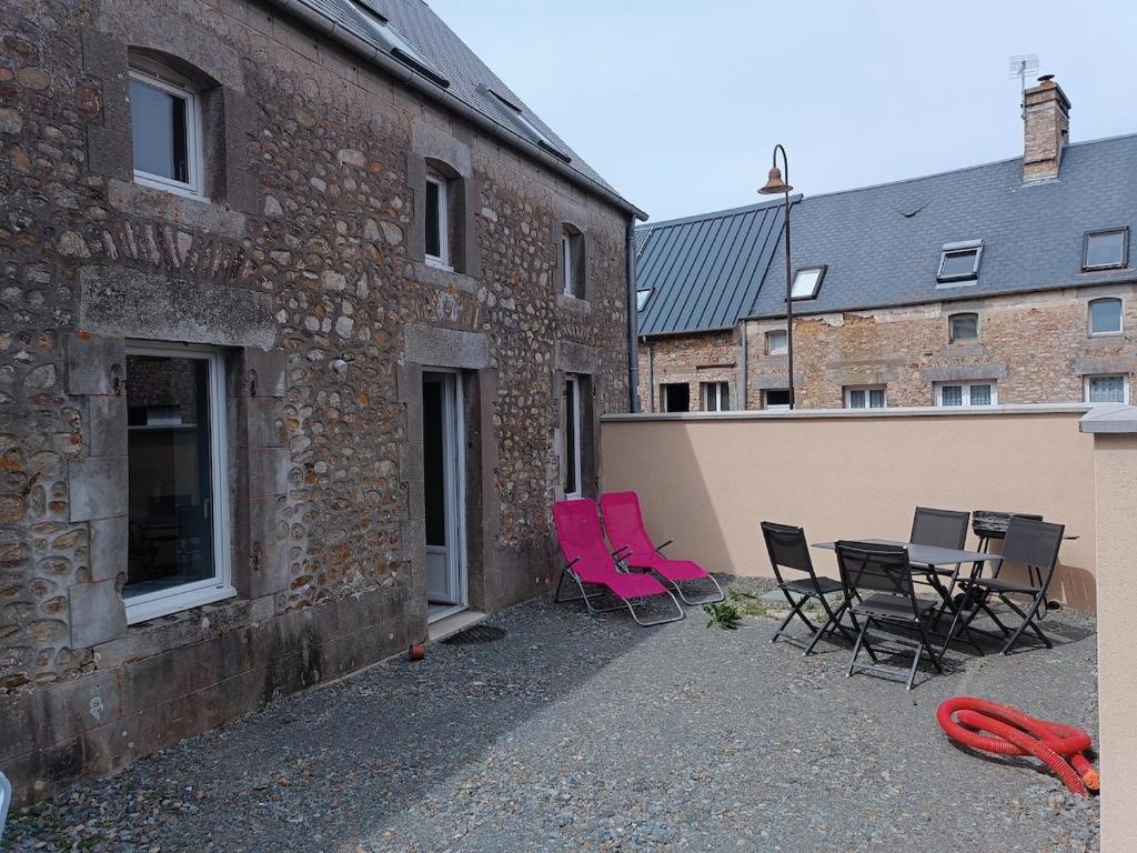 a patio with pink chairs and a table next to a building at Gite les trois Petiots in Pirou