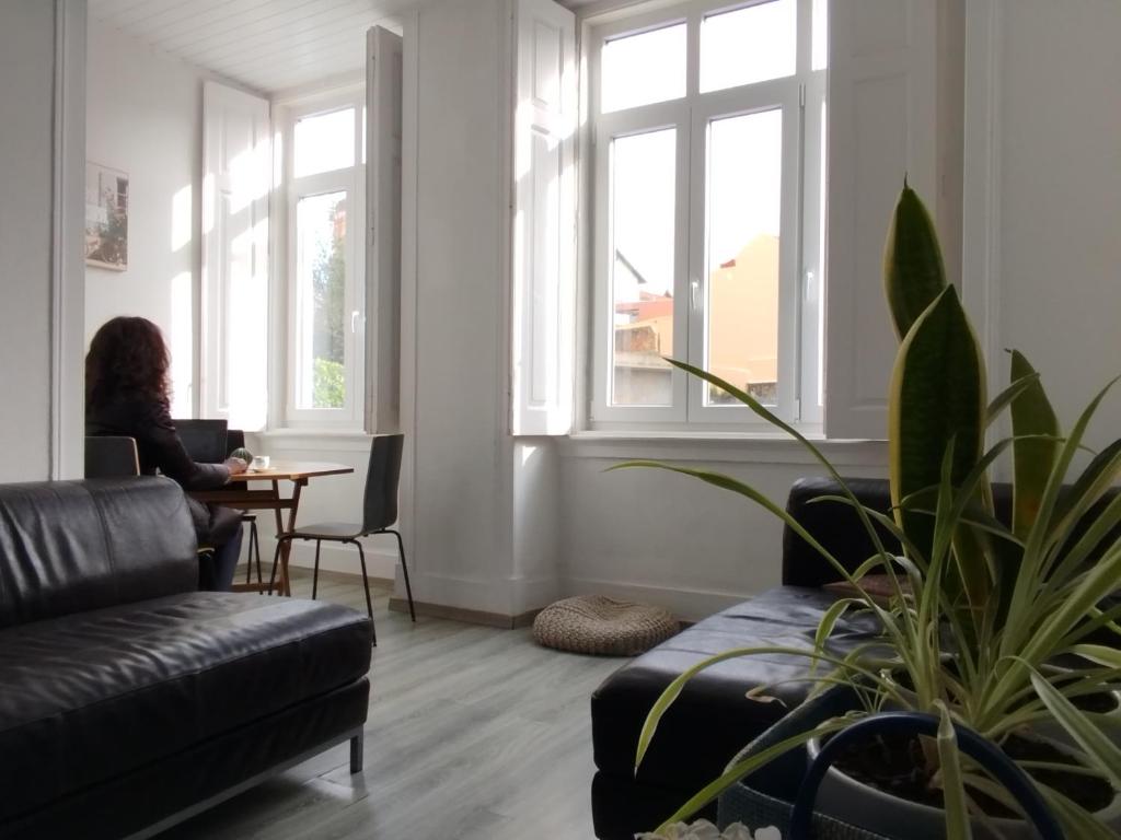 a woman sitting at a table in a living room with windows at Change The World Hostels - Cascais - Estoril in Monte Estoril