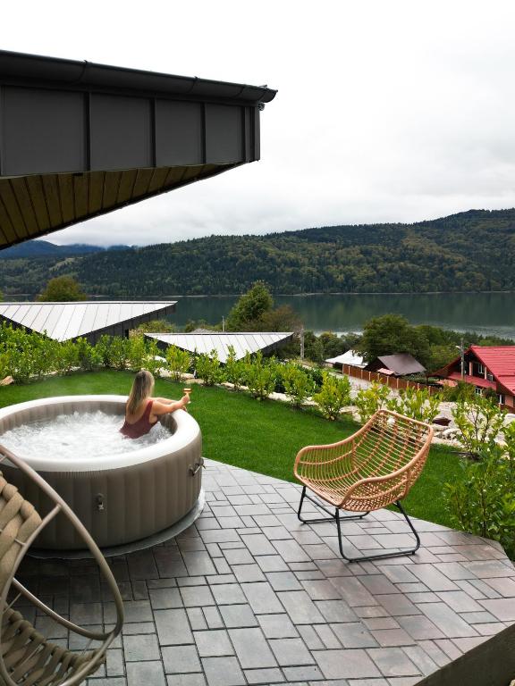 a woman sitting in a hot tub on a patio at Amumi Lacul Bicaz - Casuta Infinity in Buhalniţa