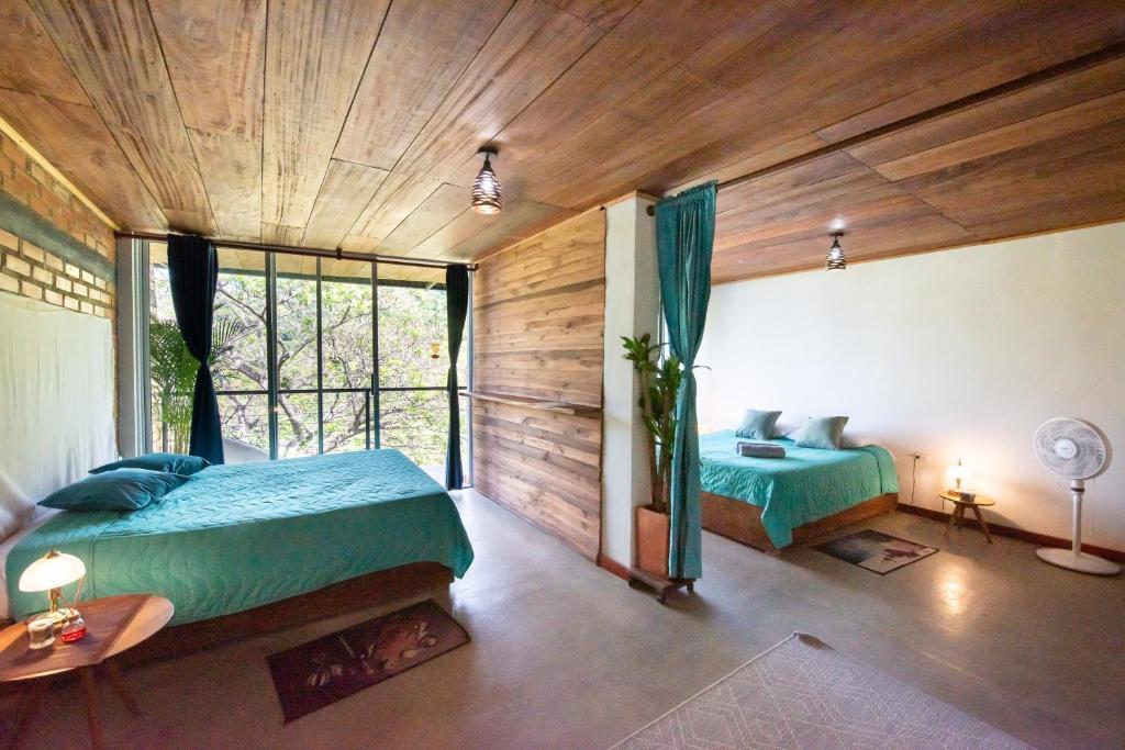 two beds in a room with wooden ceilings and a window at Pistacho in Minca