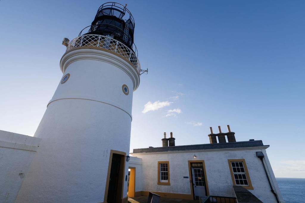 a lighthouse on top of a building next to the ocean at Principal Keeper's Cottage at Sumburgh Lighthouse, Shetland Islands in Sumburgh