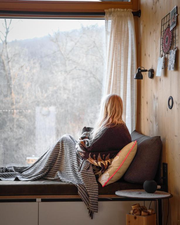 a woman sitting on a window sill looking out at Cabin Westerwald Sauna, 5G Internet, E-Ladesäule in Niederdreisbach