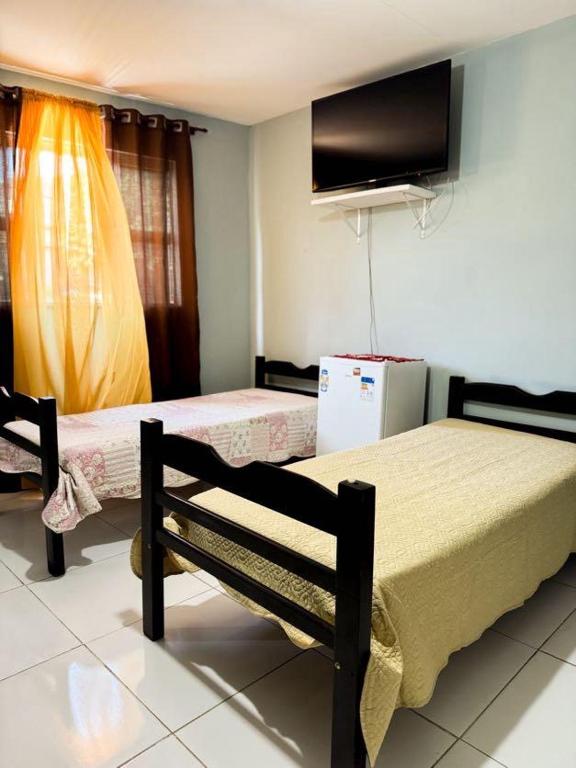 a bedroom with two beds and a tv on the wall at Suítes em Bacaxá Saquarema in Saquarema