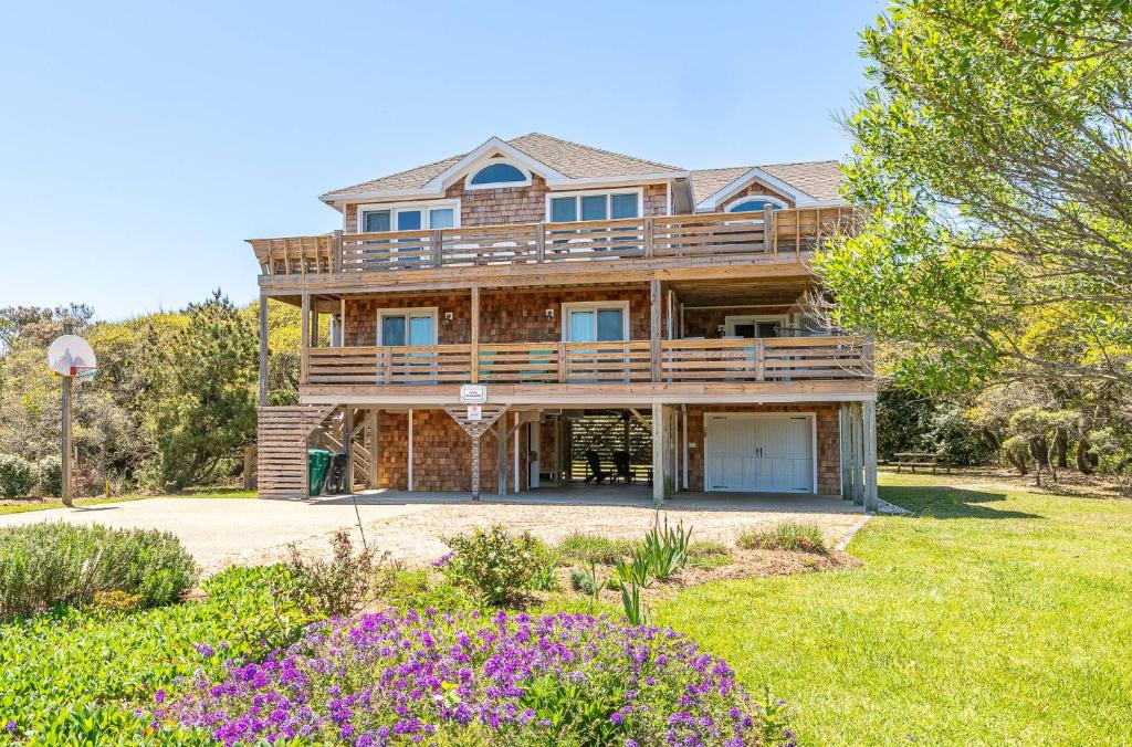 a large wooden house with a yard with flowers at Duck Diamond - Sanderling, Ocean View, 95 Yds to Beach, Hot Tub, Sauna, Community Pool in Duck