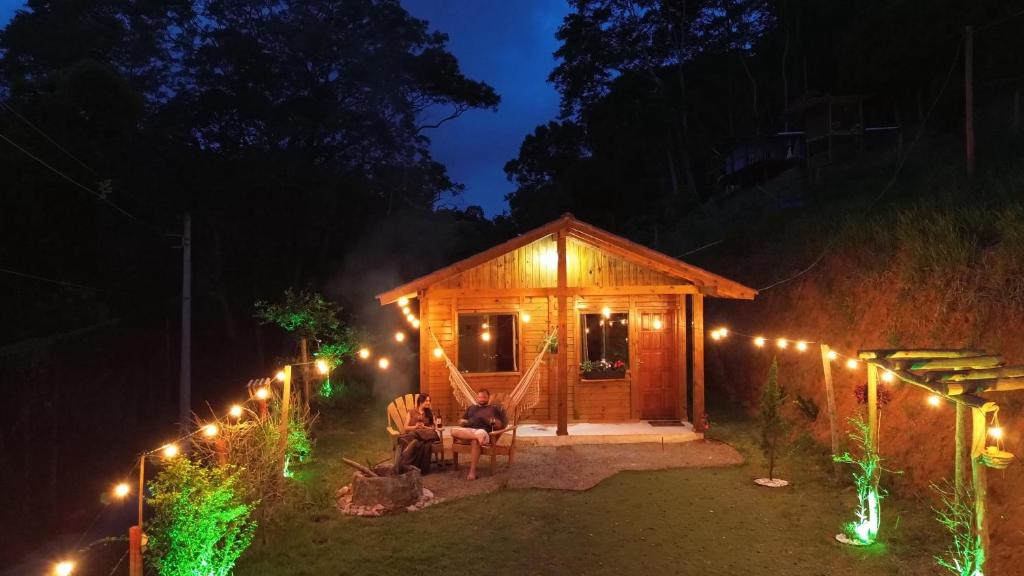 a man sitting in front of a wooden cabin with lights at Cabana Pouso Sereno in Domingos Martins