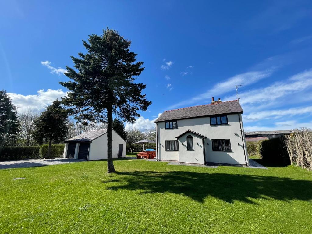 a white house with a tree in a field at The Farmhouse at Moss Bank Farm in Wrexham