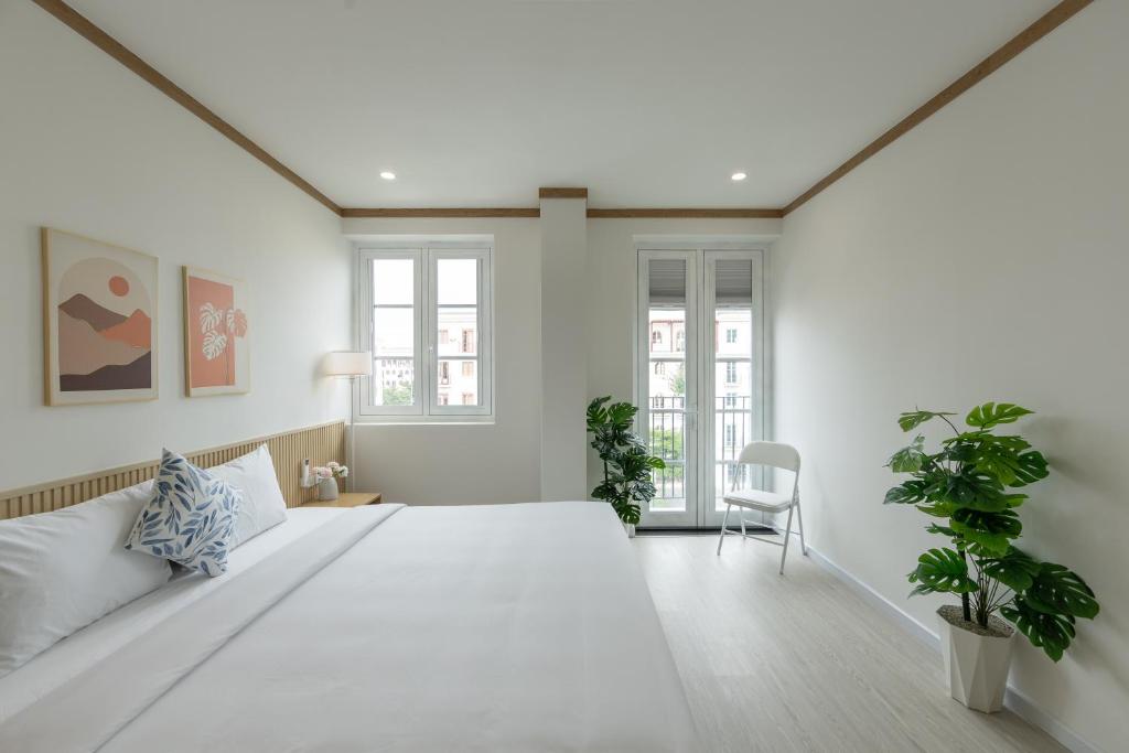 a white bedroom with a large bed and two plants at KOA Apart Hotel Phu Quoc in Phú Quốc