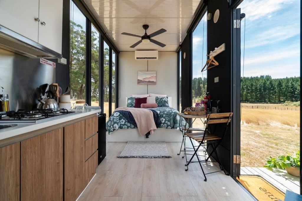 a bedroom with a bed and a kitchen with windows at Tiny Divine Farmstay by Tiny Away in Korweinguboora