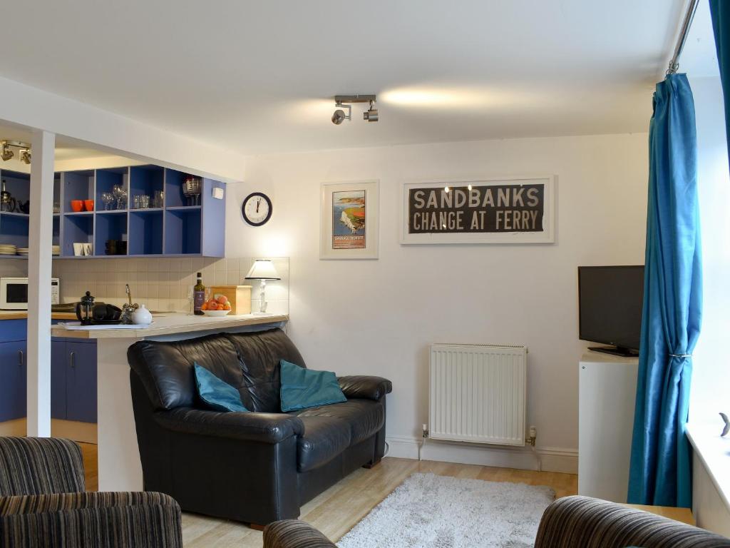 a living room with a leather chair and a kitchen at Windjammer Cottage in Swanage