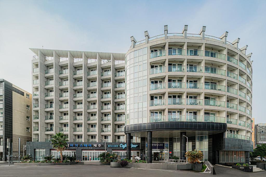 a large white building with a round building at Hamdeok Beach Stay Jeju in Jeju