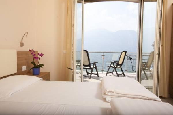 - une chambre avec un lit et un balcon avec des chaises dans l'établissement Hotel Garnì Vela d'oro, à Brenzone