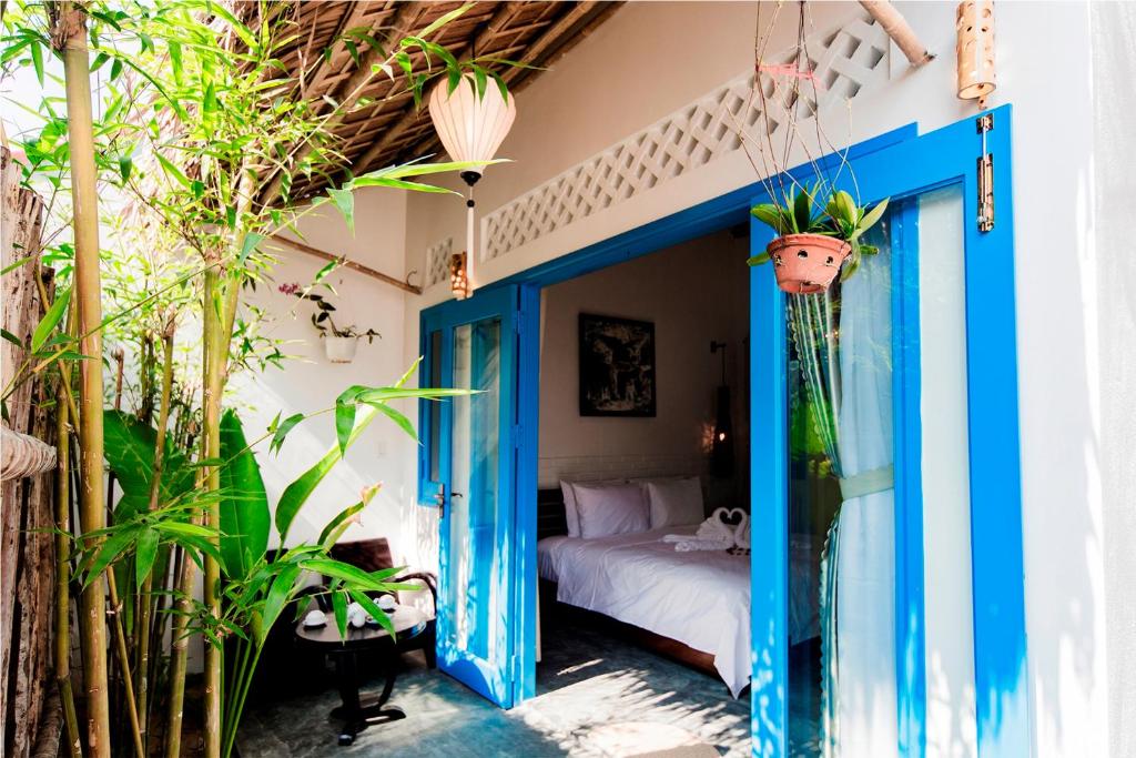 une chambre avec une porte bleue, un lit et des plantes dans l'établissement Cashew Tree Bungalow, à Hội An