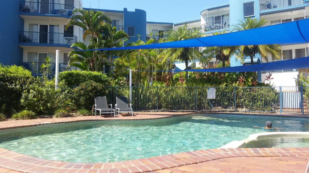 a swimming pool with two chairs in front of a building at Tranquil Shores in Caloundra