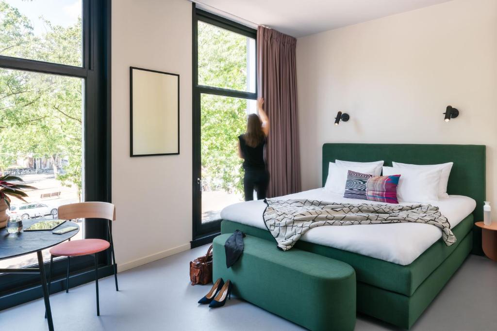 a bedroom with a green bed and a woman looking out the window at hotel emma next in Rotterdam