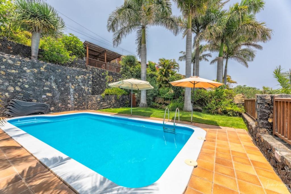 a swimming pool with an umbrella and palm trees at Guestready - La Morita Villa de Mazo in Mazo