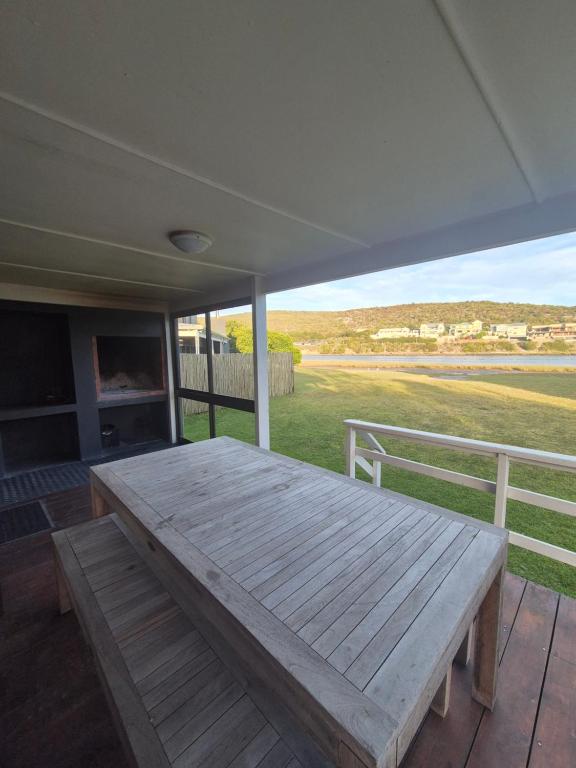 a wooden table on a porch with a view of a field at A Rickety River House in Stilbaai