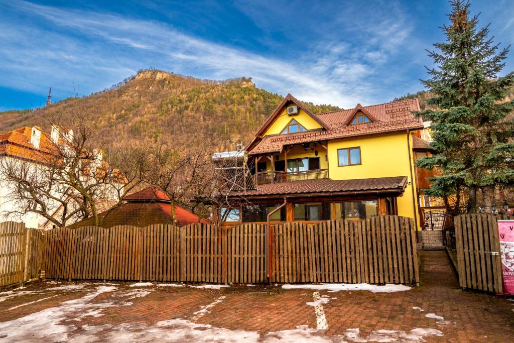 a yellow house with a fence and a mountain at Pension Brasovu Vechi in Braşov