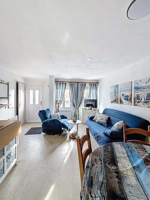 Una sala de estar con un sofá azul y una mesa. en Maison des dunes, en Fort-Mahon-Plage