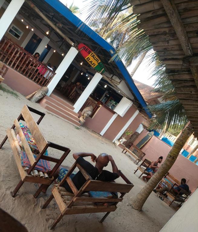 a man sitting in a chair on the beach at Dizzy Lizzies Beach House Resort in Kokrobite