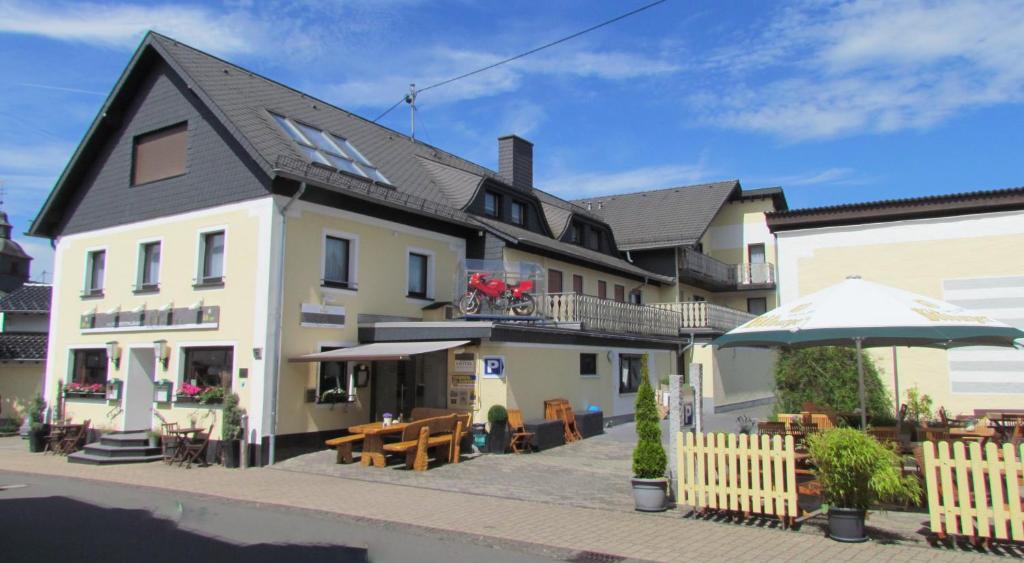 un grand bâtiment blanc avec des tables et un parasol dans l'établissement Hotel & Restaurant Hüllen, à Barweiler