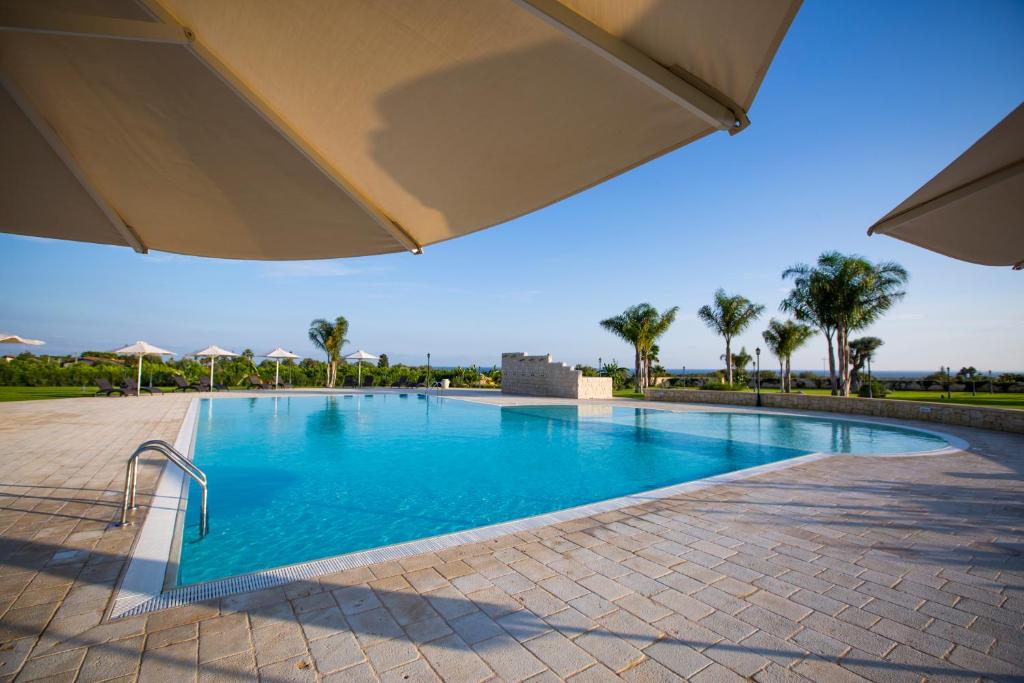 a swimming pool with an umbrella and palm trees at Casal Sikelio in Cassibile