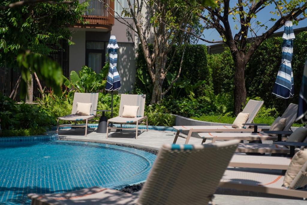a group of chairs and umbrellas next to a swimming pool at Lovely 2 Bdr Canvas BangTao in Laguna Phuket
