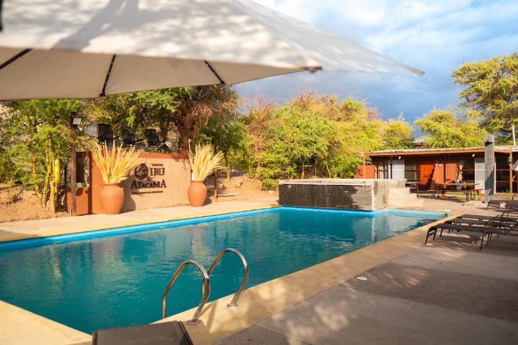 a swimming pool with an umbrella next to a house at Hostel Qiru Atacama in Sólor