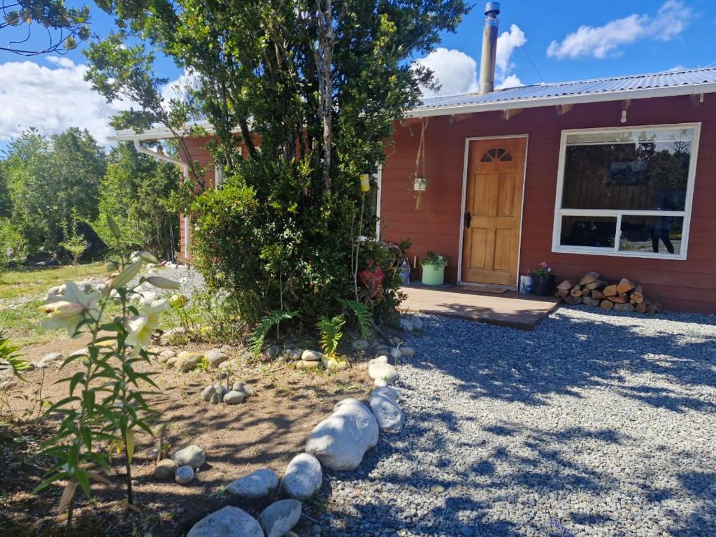 a house with a tree and rocks in front of it at Cabaña Los Notros in Colonia Alerce