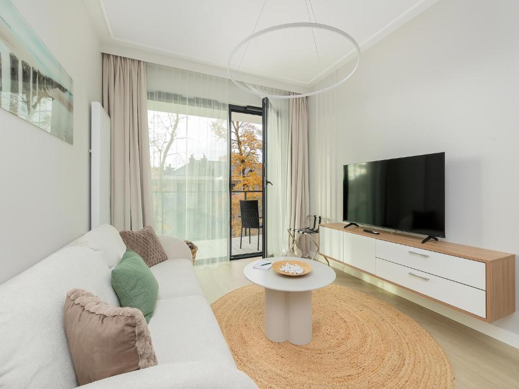 a white living room with a white couch and a tv at Comfortable apartment, right on the beach in Niechorze