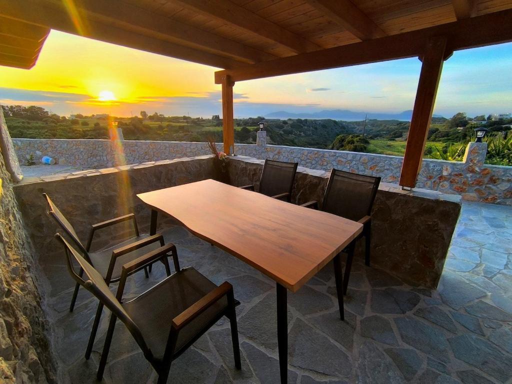 a wooden table and chairs on a patio with the sunset at Glyki Canyon Bungalow in Antimácheia