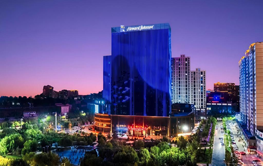 a city skyline at night with a tall building at Howard Johnson Great Eagle Plaza Aksu in Aksu
