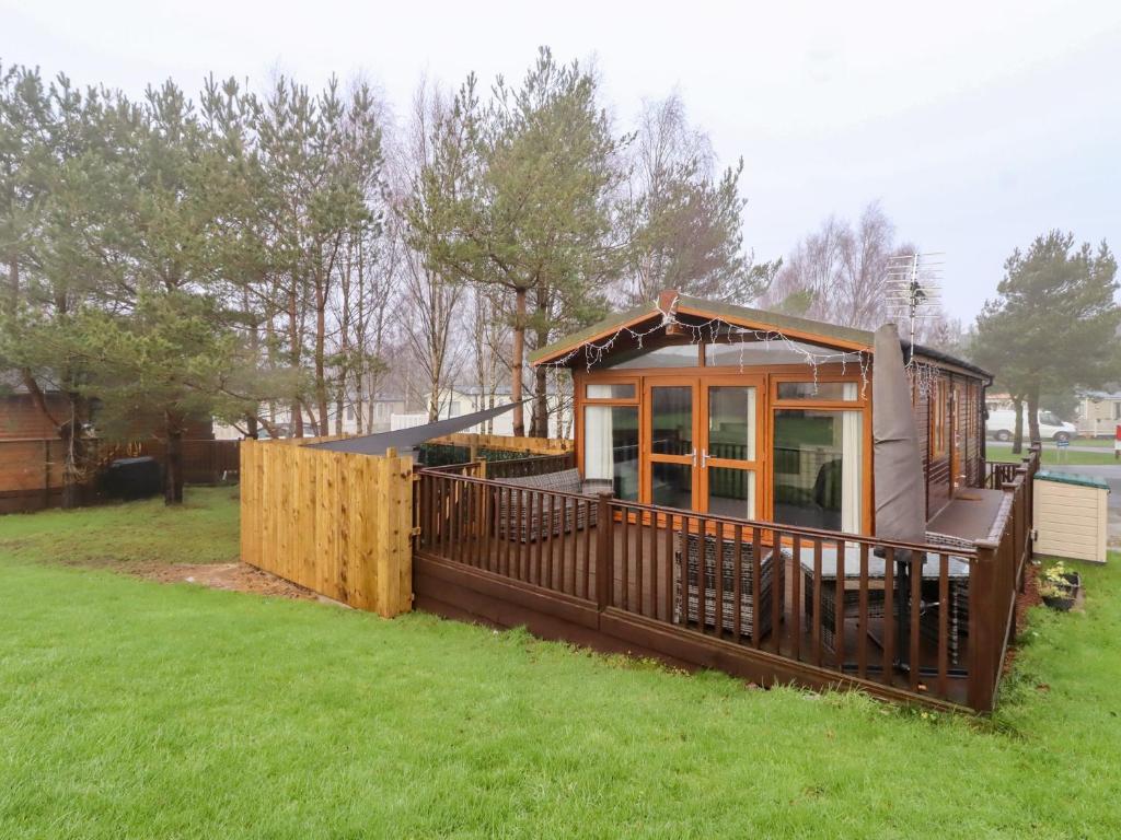 a small house with a deck in the grass at Harper's Hideaway in Morpeth