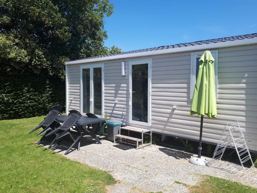 a grey caravan with a table and a green umbrella at Mobilehome Super Mercure 2 Bedrooms Comfort Camping Scheldeoord in Baarland