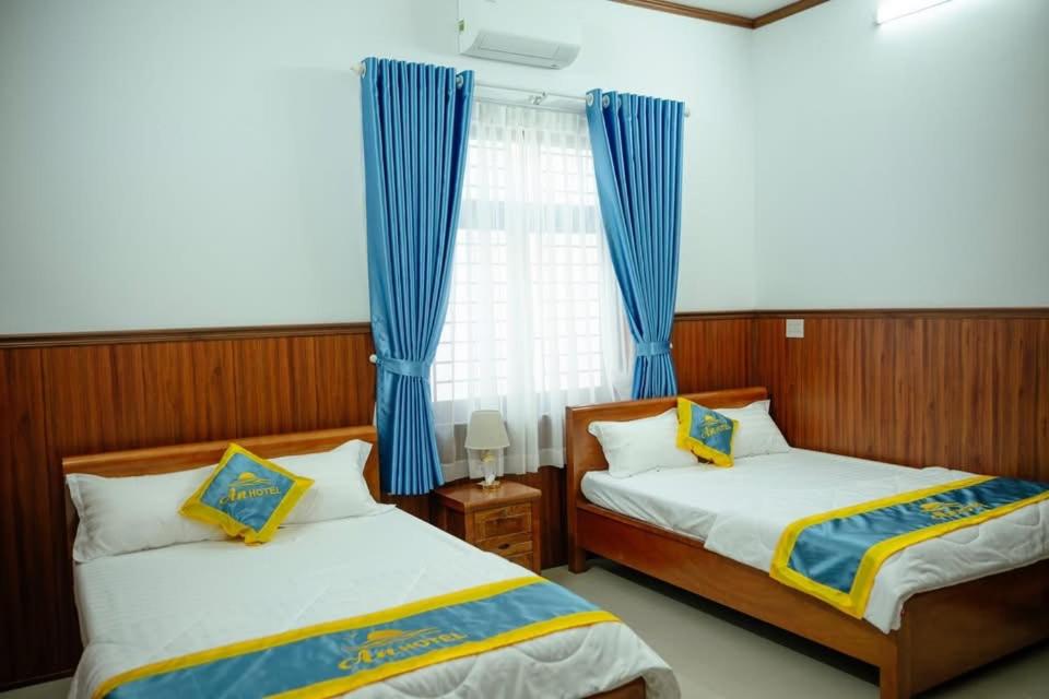 two beds in a room with blue curtains at An Hotel in Xóm Vĩnh Thanh