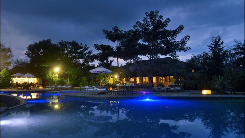 Una piscina de noche con mesas y sombrillas. en Barahi Jungle Lodge, en Meghauli