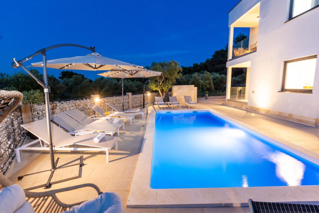 a swimming pool with chairs and an umbrella next to a house at Villa Mauro in Božava