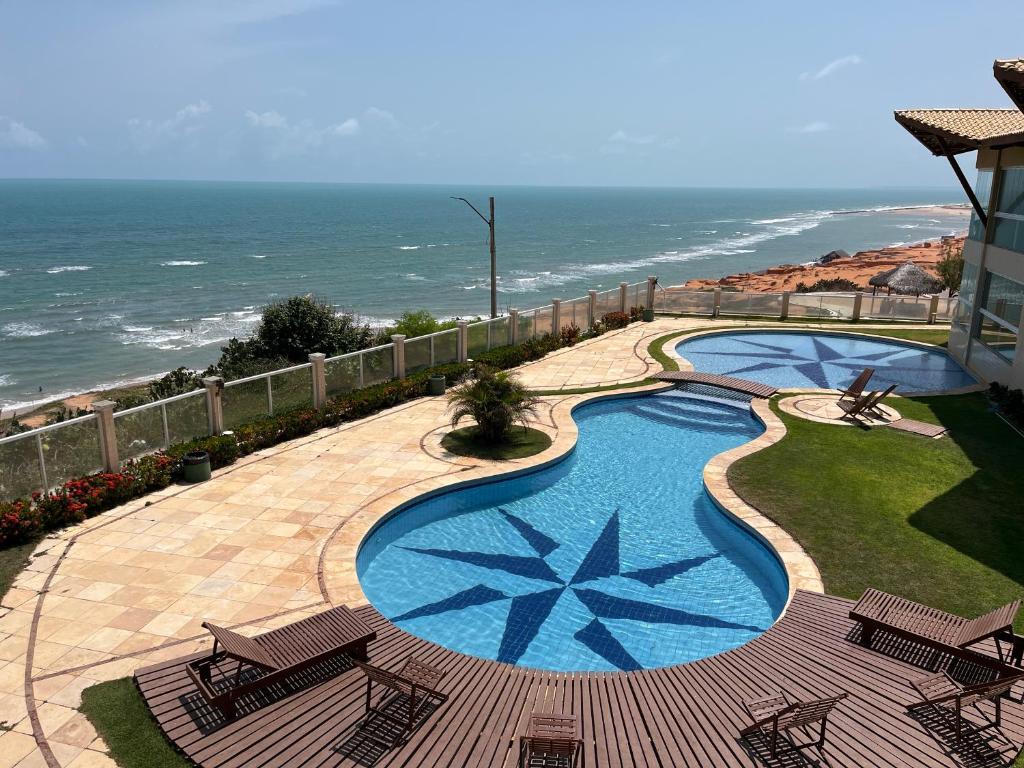 a swimming pool with chairs and the ocean in the background at Vizinho dos Parapente - Novo Luxo apartamento in Canoa Quebrada