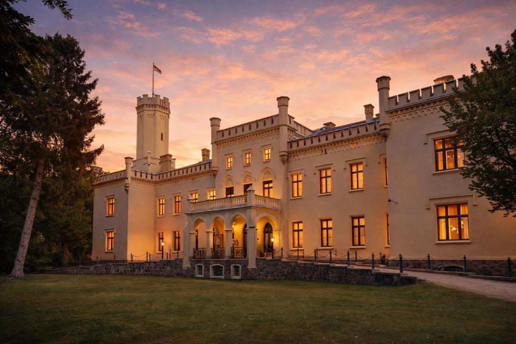 a large white house with a sunset in the background at Romantik Hotel Schloss Reichenow in Reichenow