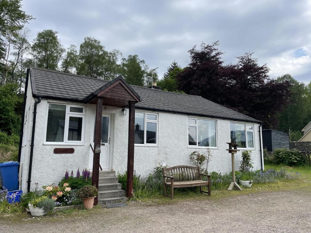 a small white house with a bench in front of it at Crianlarich Cottage in Fort Augustus