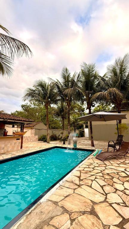 a swimming pool with palm trees and an umbrella at Recanto da Mari in Paraty
