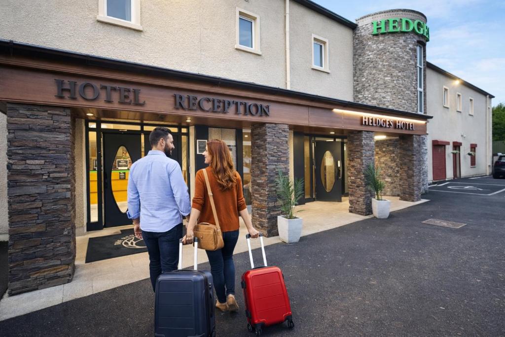 a man and woman walking in front of a hotel with luggage at The Dark Hedges Hotel in Stranocum