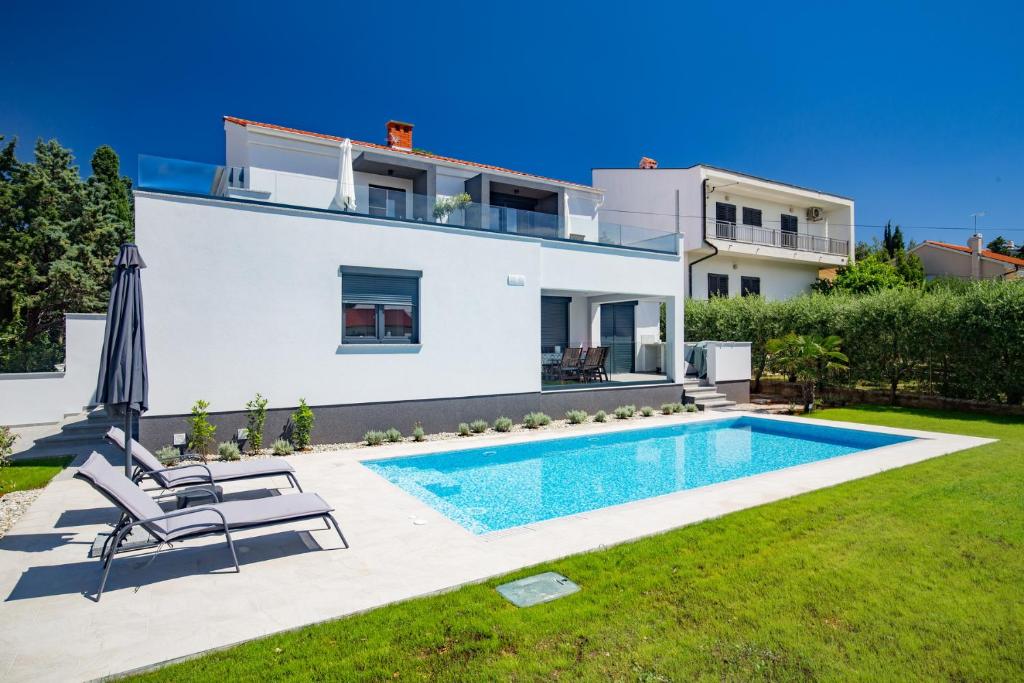 a villa with a swimming pool in front of a house at Bonihome Apartments in Punat