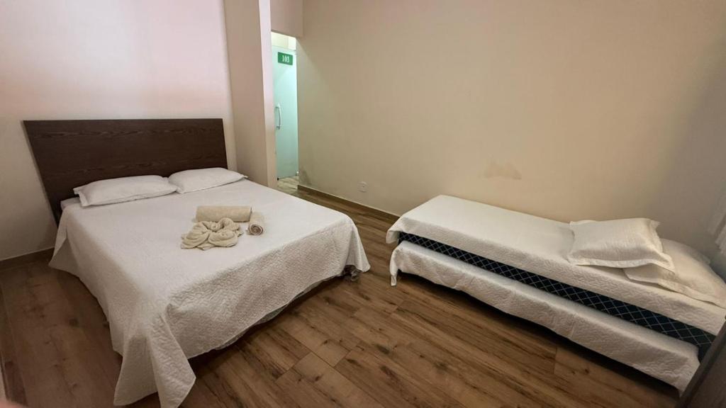 a bedroom with two beds with white sheets and a mirror at Pousada Amendoeira in Mangaratiba