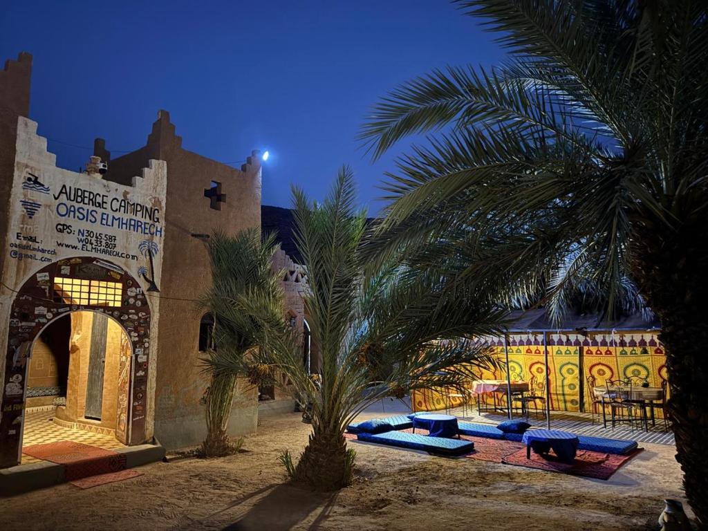 a building with a bunch of lounge chairs and palm trees at Auberge el oasis mharech in Foum Mharech