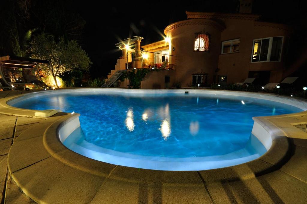 a large blue swimming pool in front of a house at night at L'Ecureuil de l'Estérel in Saint-Raphaël