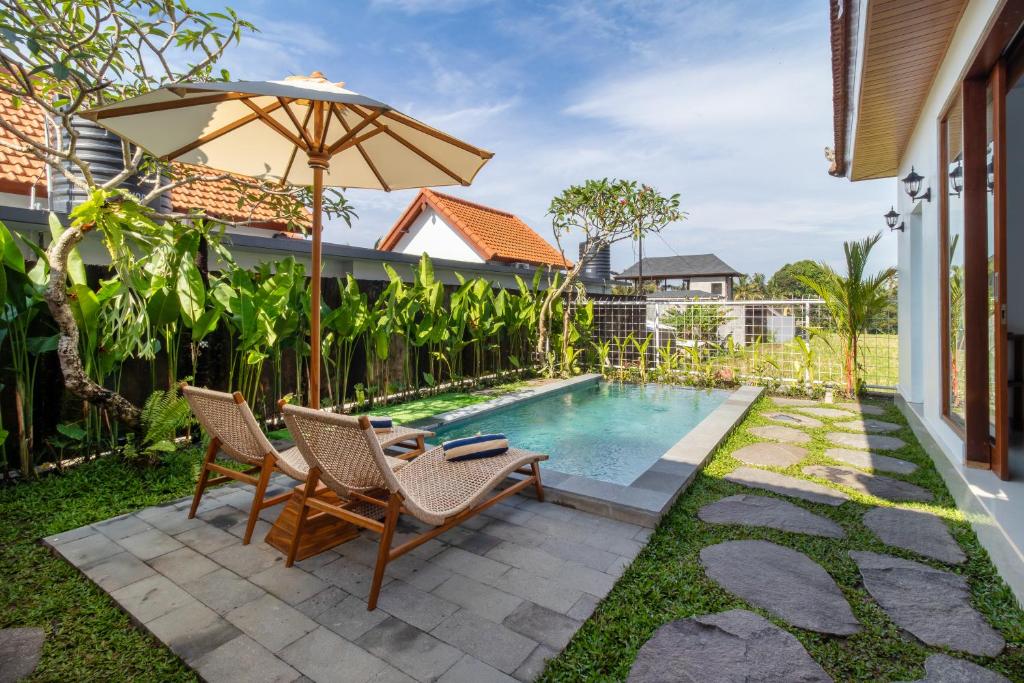 a patio with two chairs and an umbrella next to a swimming pool at Umah Uwa Villa Ubud in Tegalalang